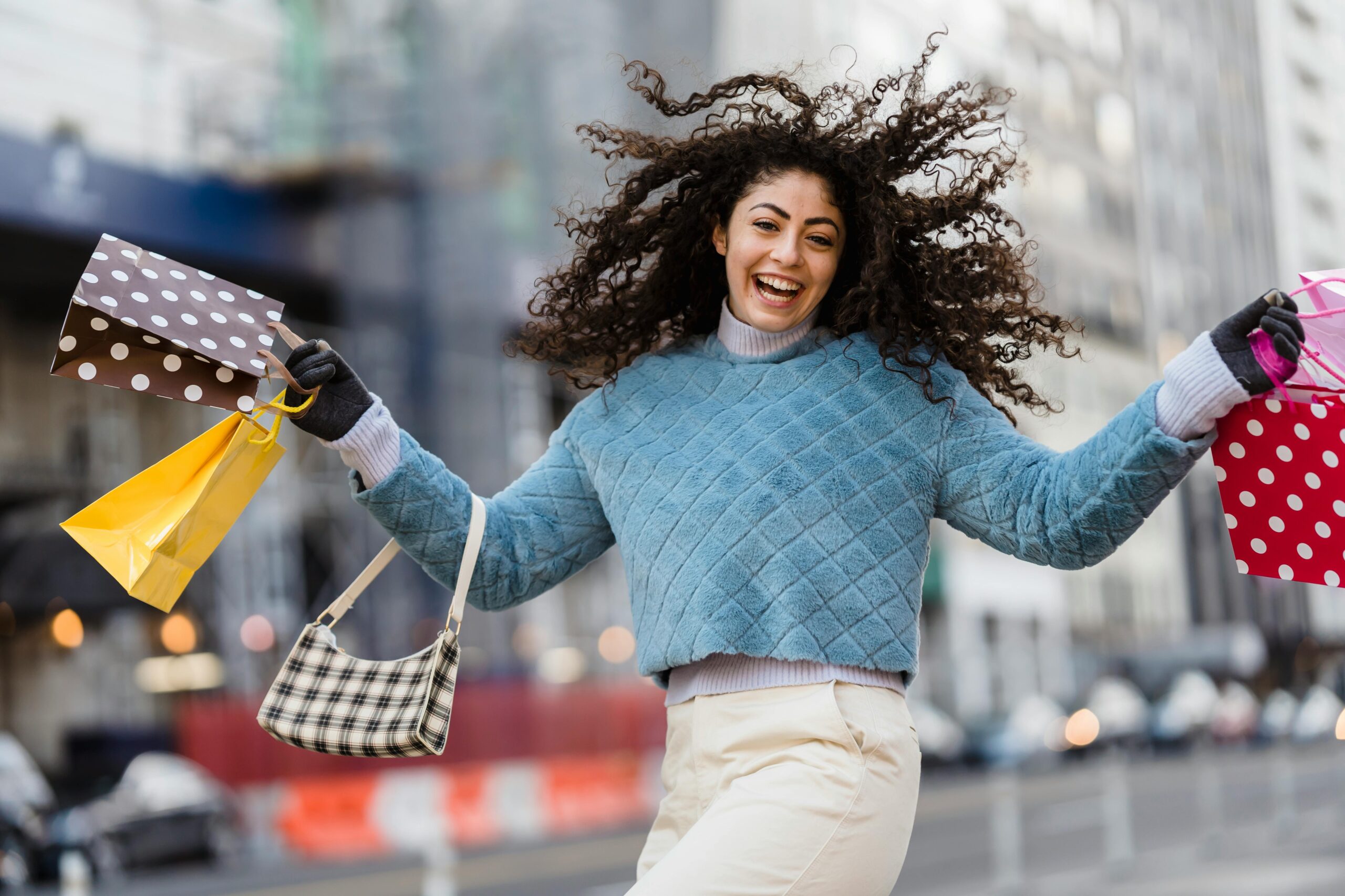 Junge Frau mit lockigen Haaren hält Shoppingtüten in der Hand und lacht