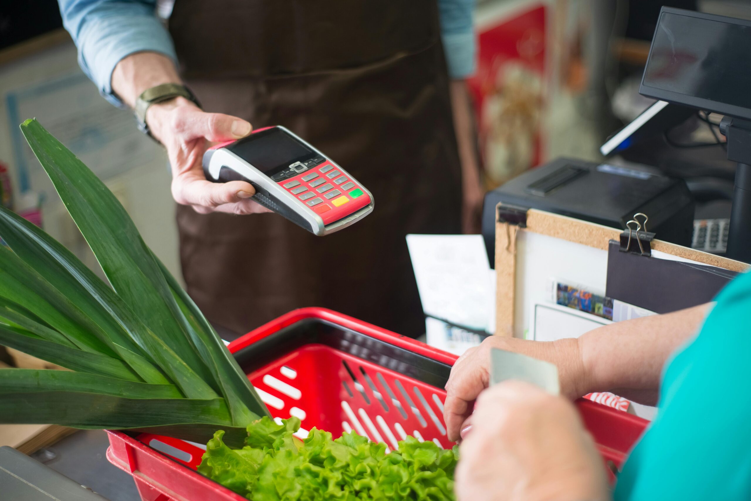 Kassierer hält einem Kunden im Supermarkt an der Kasse das Kartenlesegerät hin 